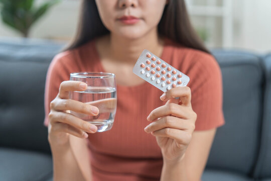 Close up woman holding oral contraceptive birth control pills blister pack and a glass of water, concept of unwanted pregnancy prevention and female healthcare.