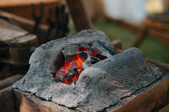 A workspace features a stone forge filled with glowing coals, surrounded by wooden tools. This setting captures the essence of medieval blacksmithing and daily life in the early Middle Ages