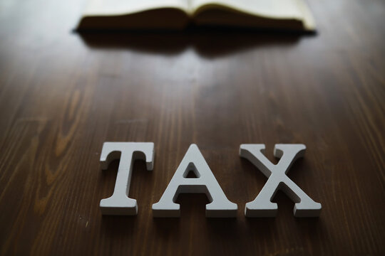 Wooden Tax Letters on Wooden Table with Open Book Background