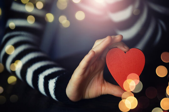 Woman holding hands with red heart on wooden background, top view