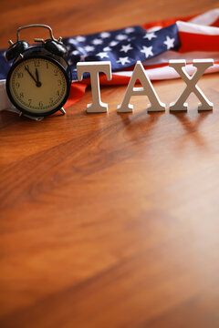 Alarm Clock and TAX Letters with American Flag Background on Wooden Table