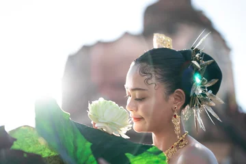 Fotobehang Lotusbloem Elegant woman in traditional attire holding a lotus flower with ornate jewelry and hair decoration outdoors  © phaitoon