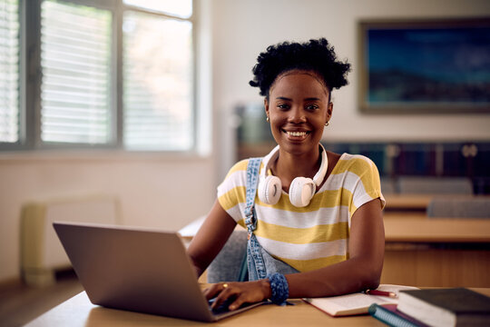 Happy black university student leaning in classroom and looking at camera.