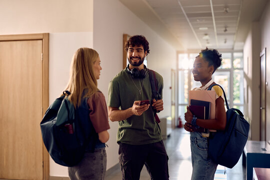 Happy college student talking to female friends in hallway.