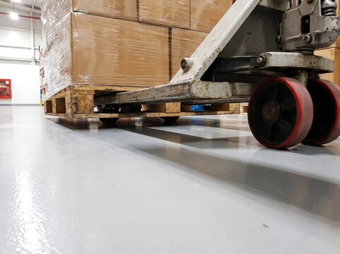 Close up of a pallet jack moving boxes on a wooden pallet in a warehouse.