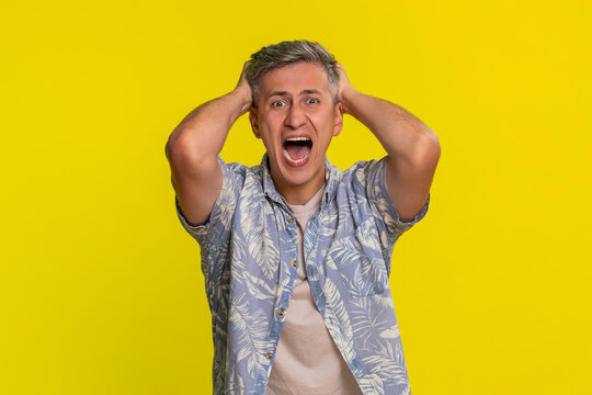 Middle-aged man shouting aggressively with wide hand gestures and furious expression, expressing strong anger and heated argument. Young guy showing emotional outburst isolated on yellow background.