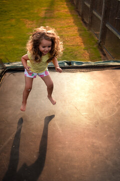 Young girl with long curly hair jumping high on trampoline