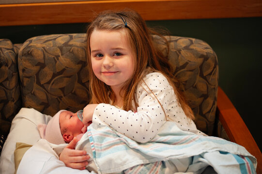 Big sister proudly holding her new baby sibling