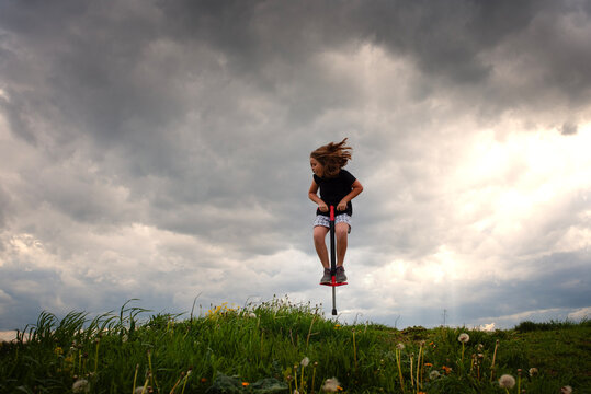 Child jumping high on a pogo stick under stormy clouds