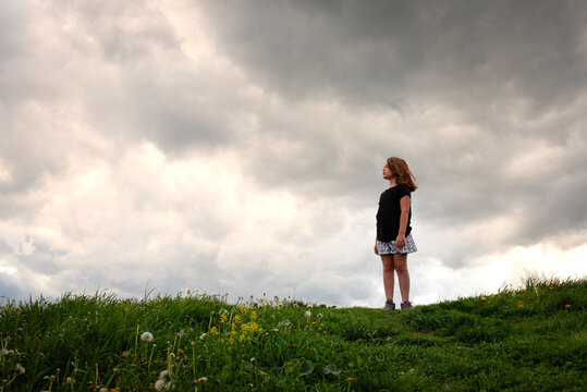Young girl standing on a hill under dramatic stormy clouds