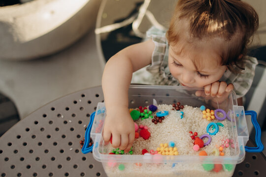 Toddler searching for hidden objects in sensory rice bin