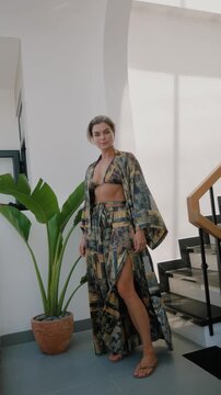 Woman modeling flowing patterned resort wear with bikini top and wide leg pants in bright modern interior.