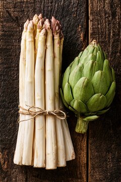 Fresh white asparagus and green artichoke on rustic wooden background