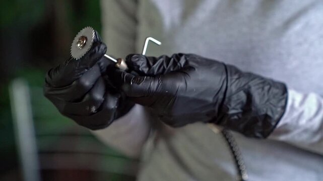 Hands in black nitrile gloves inspecting and removing circular saw blade from handheld rotary tool in indoor workshop close-up, soft diffuse light highlighting metal teeth and glossy glove texture