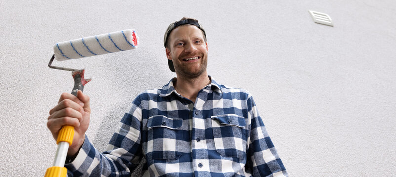 Smiling man holding paint roller ready for home painting and renovation. handyman service. copy space