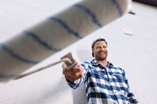 Smiling man holding paint roller ready for home painting and renovation