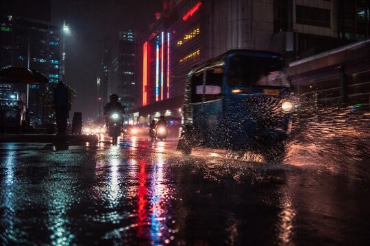 Rainy night in Jakarta with neon lights reflecting on wet asphalt as bajaj passes by