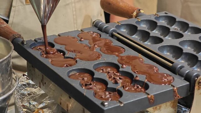 Chocolate liquid dough poured waffle iron machine to cooking waffles with sticks.