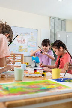Diverse students coloring on painting board on table at elementary school. 