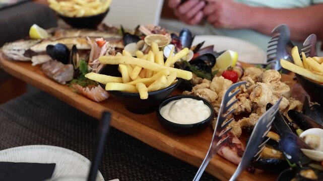 Generous seafood platter serves grilled fish shrimp mussels fried squid and french fries with lemon and creamy sauce creating an appetizing restaurant dinner for sharing
