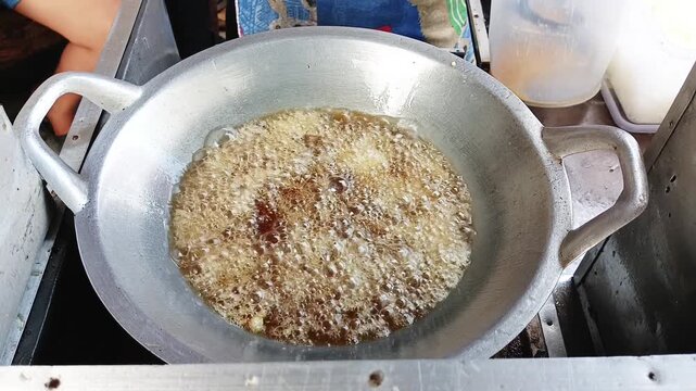 Hot vegetable oil bubbling in a large metal wok for deep frying street food called Telur Gulung in Indonesia
