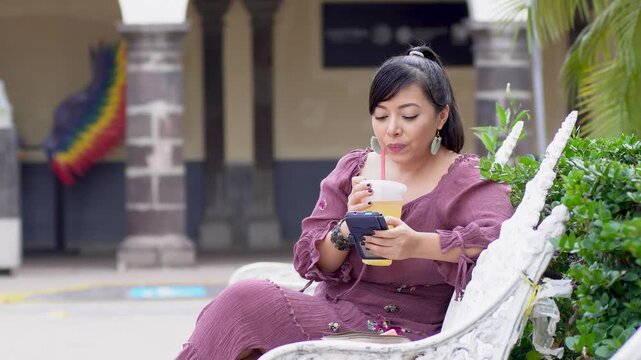 Woman Sitting on Park Bench Checking Smartphone While Drinking Orange Juice