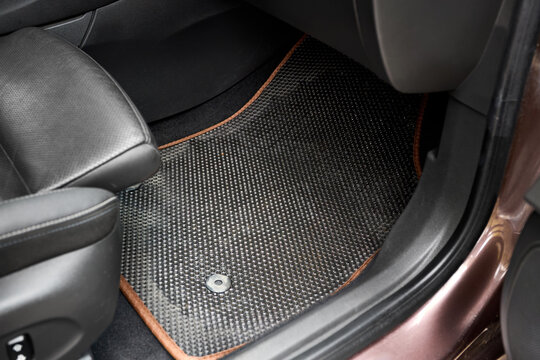 Black EVA material car floor mat with brown borders placed in vehicle interior. Cellular structure grid traps dirt, water, dust. Protects vehicle carpet. Clean modern auto styling accessories.