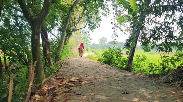 Narrow brick and soil pathway in rural village with green trees and walking villager