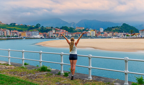 woman standing with arms open enjoying scenic view of ribadesella coastal town in asturias spain
