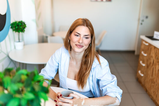 Coffee break at office canteen. Relaxing pause and refreshment, Smiling woman holding cup at white table in modern cafeteria. Attractive employee resting during break.