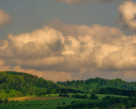 Warm golden sunlight illuminating fluffy clouds rolling over green hills and countryside