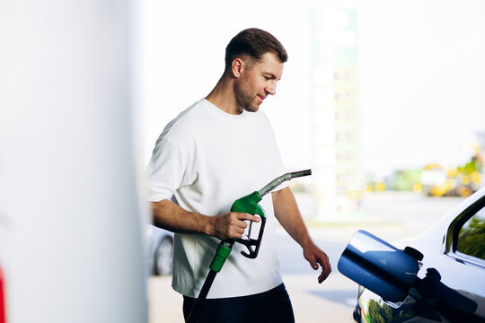 Man holding a green fuel nozzle, filling up his car at a gas station, focusing on energy, transportation, and service