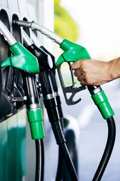 Hand holding a green fuel nozzle, preparing to refuel a vehicle at a gas station, highlighting energy and transportation