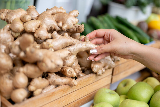 Close up of a woman's hand buying or selecting a fresh ginger from produce display at local market.