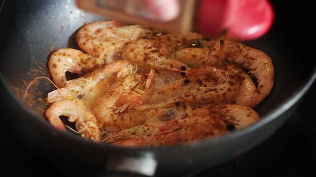 Sprinkling paprika to pan with frying tiger prawns. Shrimps cooking. Food prep.