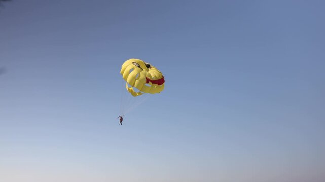 Close view of a tourist parasailing high in a clear blue sky beneath a vibrant yellow parachute enjoying an exciting summer water sport and aerial adventure over the sea
