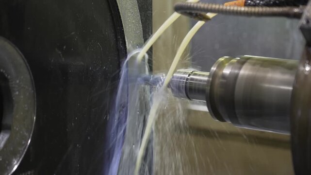 Coolant fluid spraying over a rotating steel shaft during cylindrical grinding on an industrial precision grinder machine