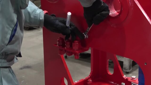 Assembly worker tightening large bolts with a wrench on a freshly painted red steel frame of construction machinery