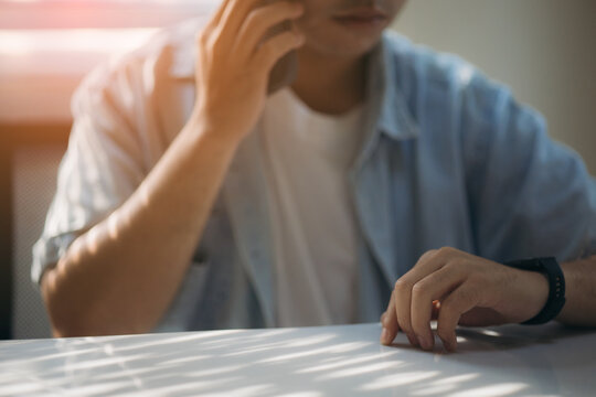 Close-up of a person talking on a mobile phone while seated at a table in a softly lit indoor environment, casual attire, contemplative mood, natural light