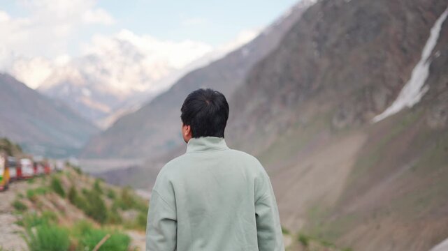 4K Rear view shot of an Indian male tourist walking in front of snow covered Himalayan mountain peaks during the summer season at Darcha in Lahaul and Spiti district, Himachal Pradesh, India.