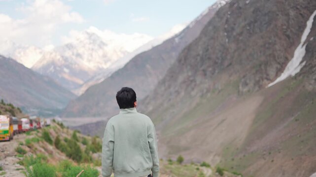 4K Rear view shot of an Indian male tourist looking at the snow covered Himalayan mountain peaks during the summer season at Darcha in Lahaul and Spiti district, Himachal Pradesh, India.