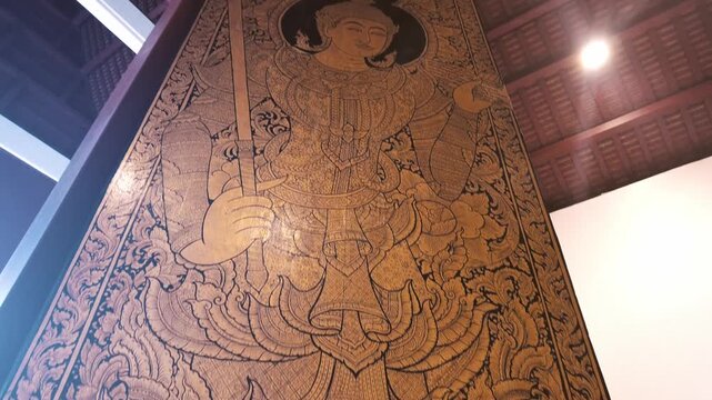 Huge temple door traditional Thai wood carving painted on. depicting an angel or celestial deity (devata) holding a sword.
