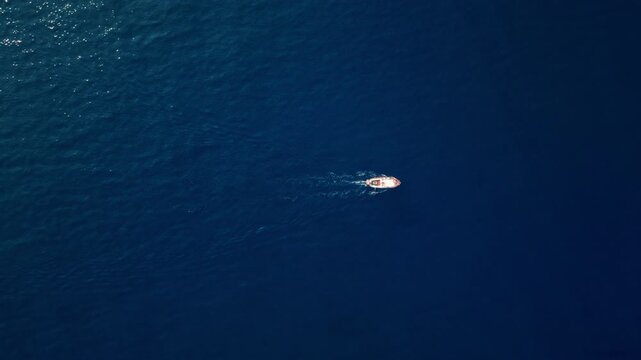 Small boat moves across calm deep blue sea viewed from above in daylight