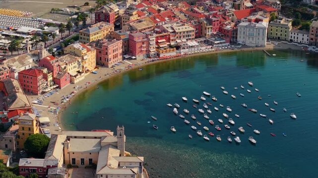 Aerial view of boats anchored in turquoise bay beside colorful Italian seaside town