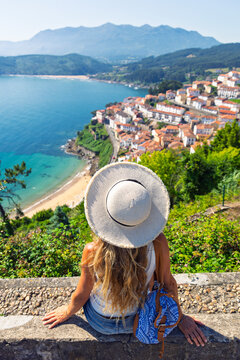 woman wearing straw hat sitting enjoying panoramic view of lastres coastal village in asturias spain