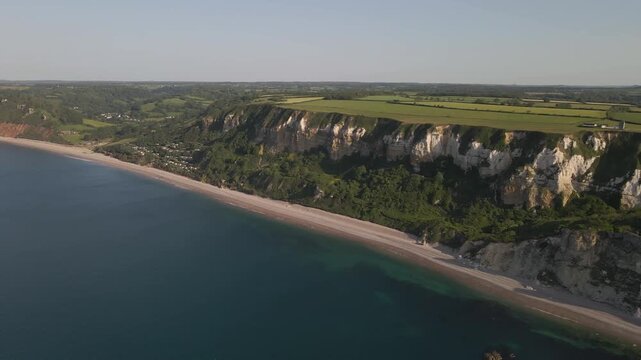 Aerial footage showcasing the White Cliffs of Seaton during calm weather, with gentle waves surrounding the rugged coastline. Overhead view captures the natural patterns of chalk cliffs and coast path