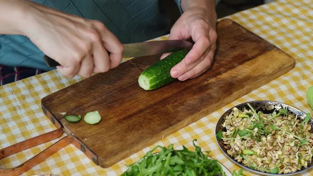 Food prep. Female hands slicing cucumber for salad on wooden board. 