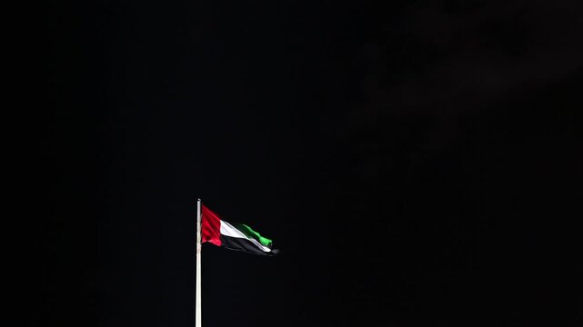 The United Arab Emirates flag waving proudly in the night sky.
