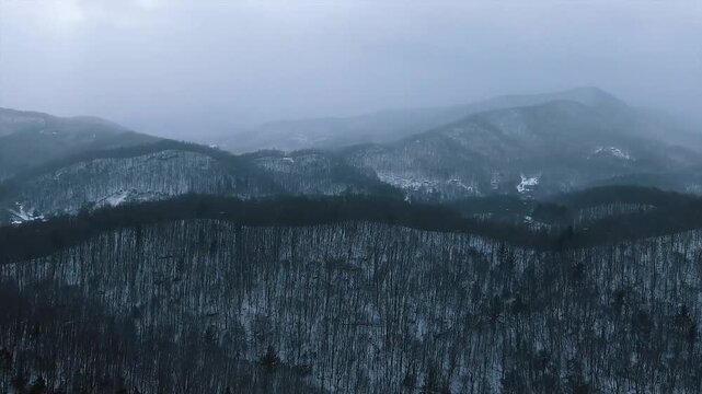 Cinematic Aerial Drone View of Snowy Mountain Ranges and Frozen Forest Under Overcast Winter Sky