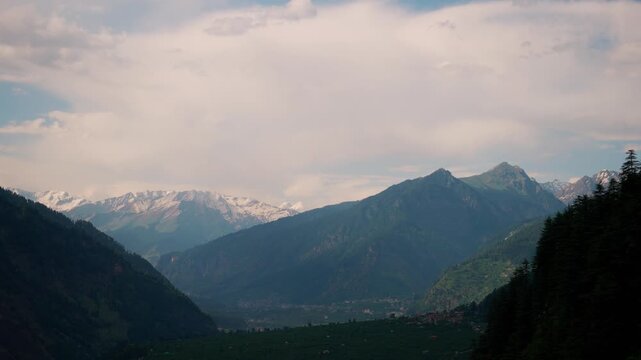 4K Landscape shot of Himalayan mountain range above Manali during the sunset in monsoon season with snow on mountain peaks as seen from Naggar in Himachal Pradesh, India. Scenic natural background.